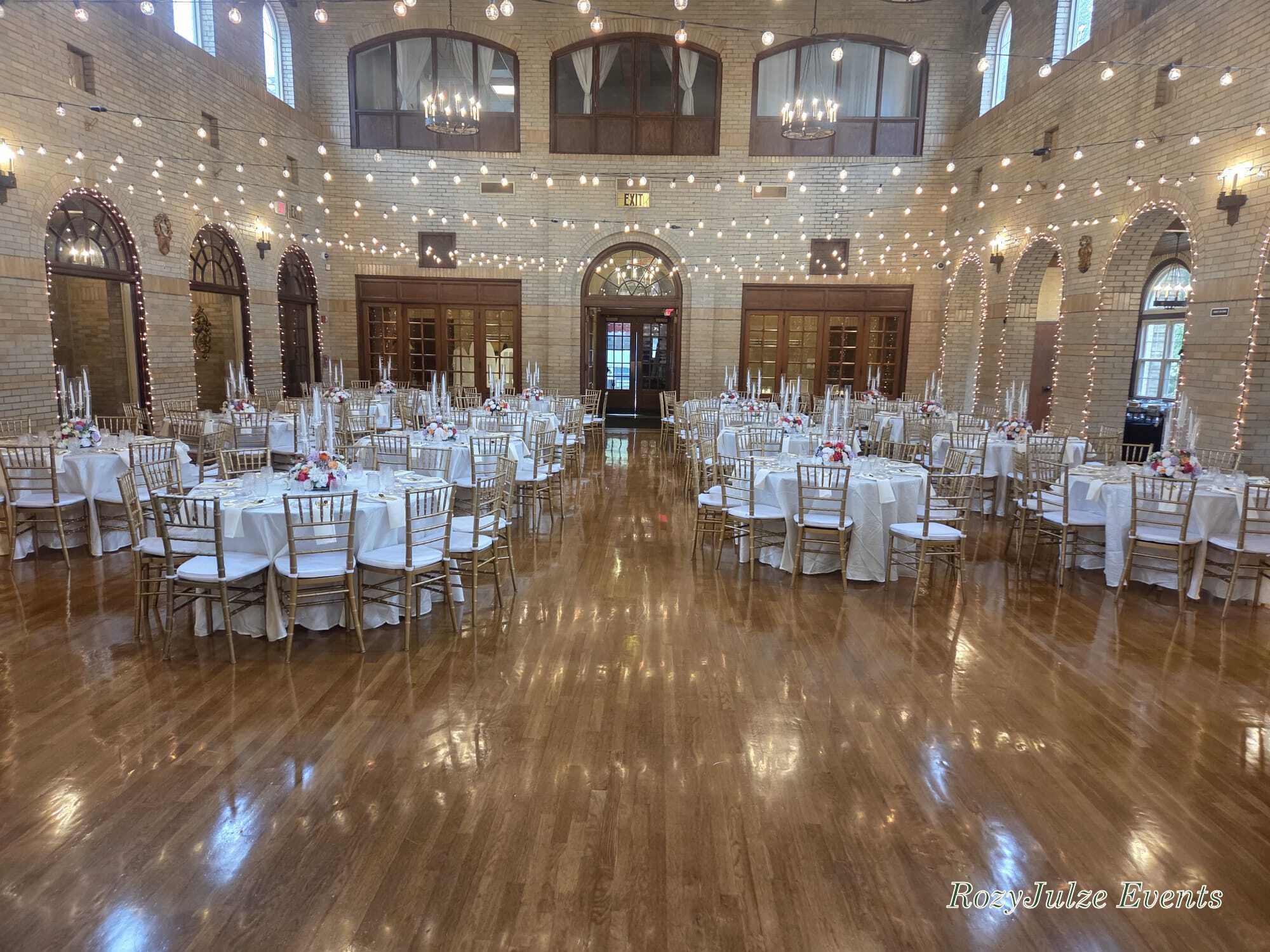 Elegant RozyJulze Events venue setup with round tables, gold chairs, floral centrepieces and a RozyJulze Events watermark
